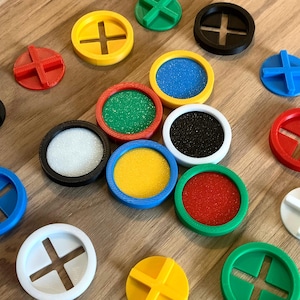 May include: Assortment of colorful round plastic discs with different textures and designs. Some discs have a cross shape in the center, while others have a textured surface. The discs are arranged on a wooden surface.