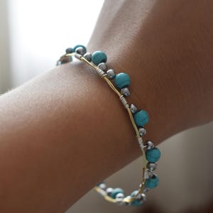 May include: A handmade bracelet featuring turquoise and silver beads strung on a gold-colored wire. The beads are evenly spaced along the wire, creating a delicate and stylish accessory. The bracelet is designed to be worn on the wrist.