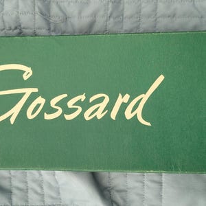 May include: A rectangular dark green cardboard box with the word Gossard printed in large cream-colored cursive script across the center. The text Youthful Line of Beauty is printed in a smaller cream-colored font along the right side of the box.
