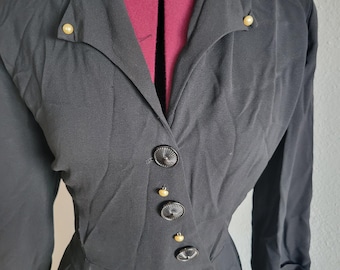 May include: A black dress with a long sleeve and a V-neckline. The dress has a row of black buttons down the front and gold accents.