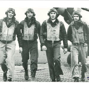 May include: Black and white photograph of four men in vintage flight gear, including helmets, goggles, and vests. They are walking on a tarmac near an aircraft. The image is signed by Bill Larson.