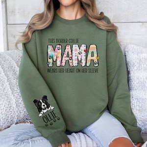 May include: Green sweatshirt with the text "This Border Collie Mama wears her heart on her sleeve" and a colorful patchwork design of the word "Mama". The left sleeve has a black and white border collie illustration with the name "Ollie" underneath.