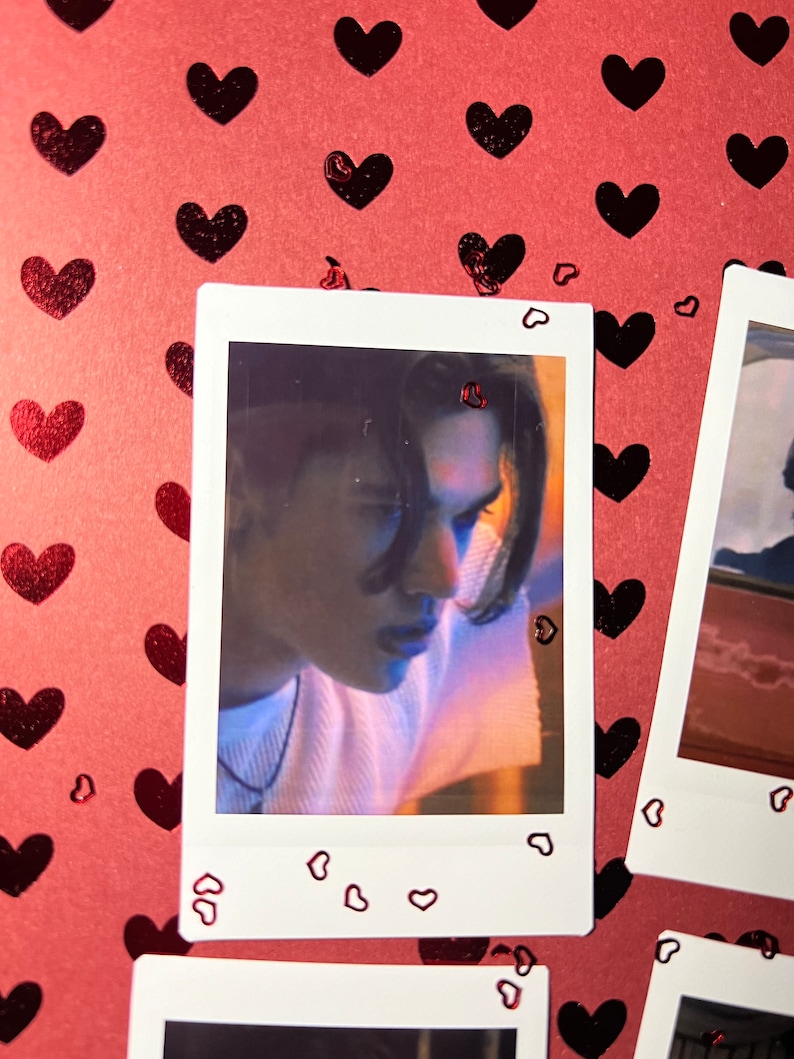 May include: A Polaroid photo of a person with long dark hair looking down. The photo is surrounded by a white border with small red hearts.