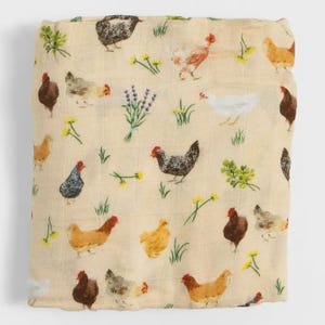 May include: Cream-colored muslin blanket with a repeating pattern of chickens in various colors, including brown, black, and white. The design also features sprigs of lavender, yellow flowers, and green foliage. The blanket is folded.