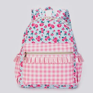 May include: A light blue backpack with a floral rose pattern and a pink gingham pocket. The pocket has a gold zipper and a pink ruffle trim. The backpack has two side pockets with pink ruffle trim.