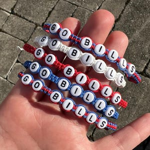 May include: Five red, white and blue friendship bracelets with the words "GO BILLS" spelled out in white beads.