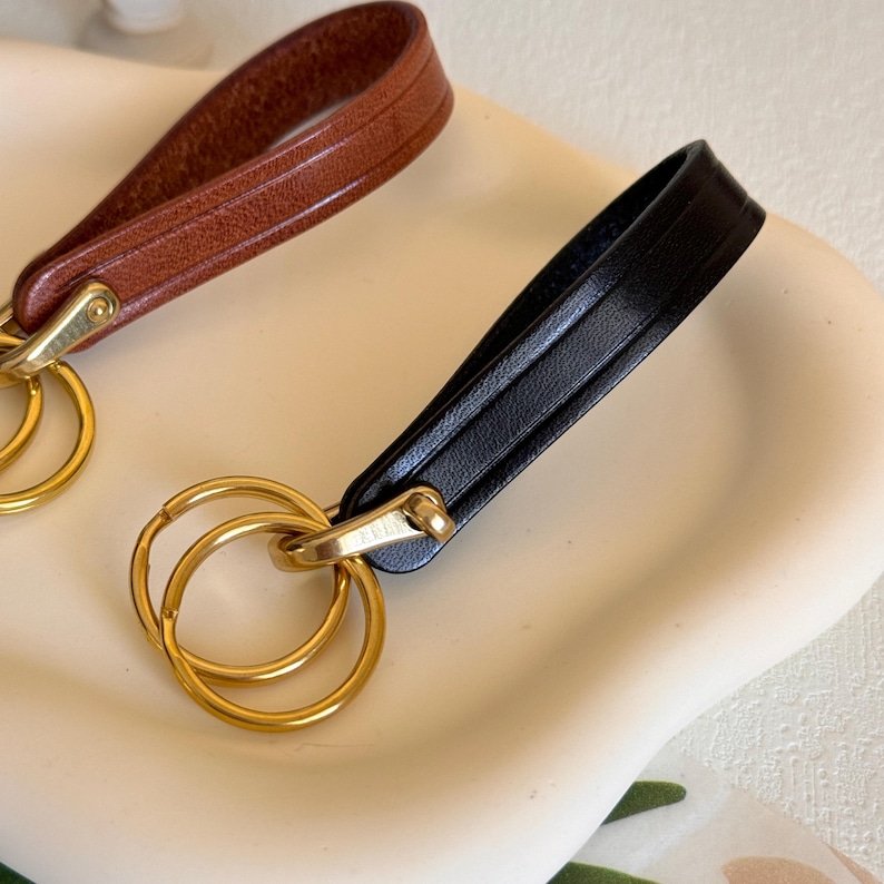 May include: Two leather keychains with gold key rings. One keychain is brown leather and the other is black leather.