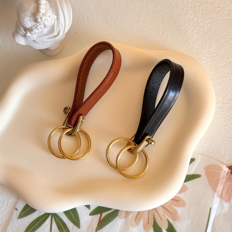 May include: Two leather keychains with gold key rings. One keychain is brown leather and the other is black leather.