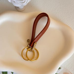 May include: A brown leather key chain with a gold metal key ring. The key chain has a loop for attaching to a belt or bag.