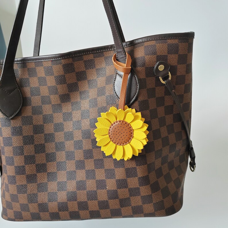 May include: A brown and black checkered tote bag with a brown leather sunflower keychain. The sunflower is yellow with a brown center.