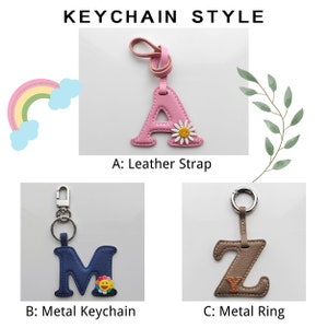 May include: The image showcases three keychain styles: a pink leather strap with the letter "A" and a daisy, a blue "M" metal keychain with a smiling flower, and a brown "Z" metal ring with a small "Y". The text "KEYCHAIN STYLE" is at the top.