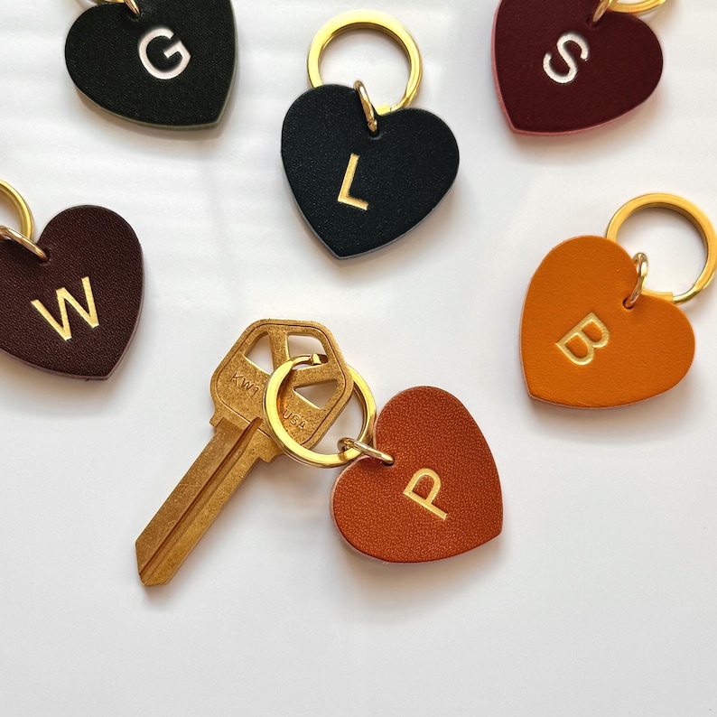 May include: Heart-shaped leather keychains in various colors, each with a gold initial. Keychains include the letters G, L, S, B, W, and P. A gold key is attached to a keychain with the letter P. The keychains have gold key rings.