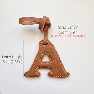 May include: A brown leather luggage tag in the shape of the letter "A" with a strap. The letter height is 2.36 inches, and the strap length is 5.9 inches. The tag has a stitched border.
