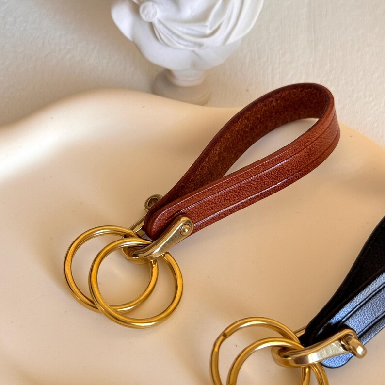 May include: Two leather keychains with gold key rings. One keychain is brown leather and the other is black leather.