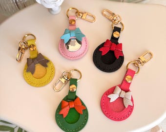 May include: Five colorful leather keychains with a bow and a clear circle for a photo. The keychains are pink, yellow, black, red, and green.