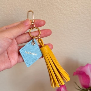 May include: A light blue leather keychain with the name "Isabelle" in gold lettering and a yellow tassel.