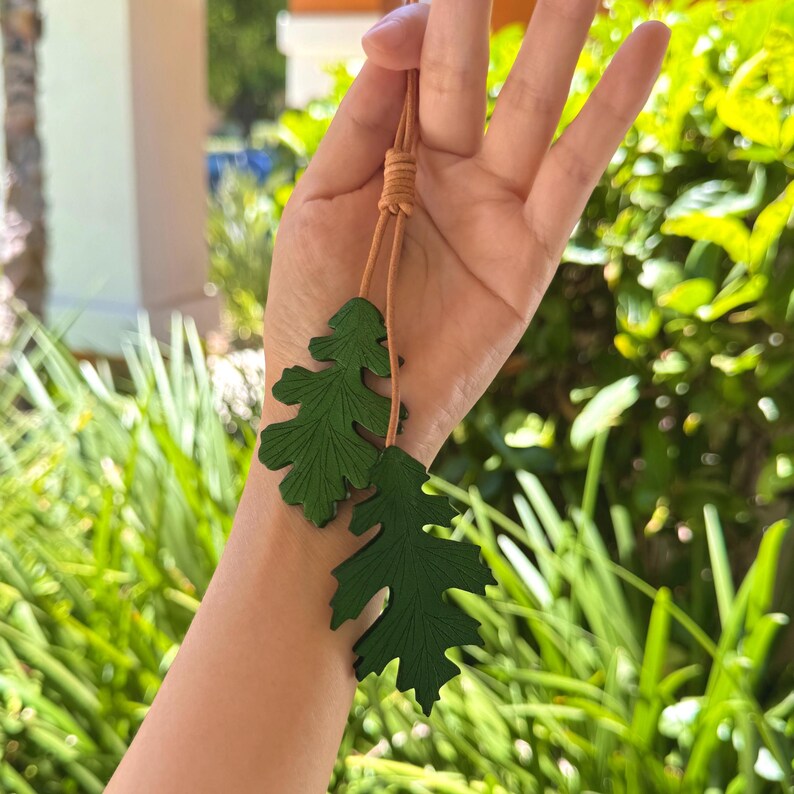 May include: A green leather necklace with two leaf charms. The necklace is made of brown leather cord and has a simple knot closure.