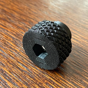 May include: Black plastic knob with a square hole in the center and a textured diamond pattern on the outside.