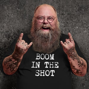 Puede incluir: Un hombre con barba larga y gafas lleva una camiseta negra con el texto "BOOM IN THE SHOT" impreso en blanco.