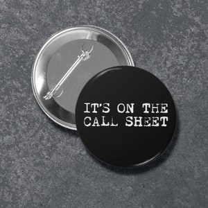 May include: Black button with white text that reads "IT'S ON THE CALL SHEET".