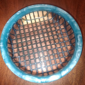 May include: A round decorative bowl with a turquoise rim and a wooden grid interior. The bowl's rim has a marbled effect, and the grid is made of dark brown wood. The bowl is set on a wooden surface.
