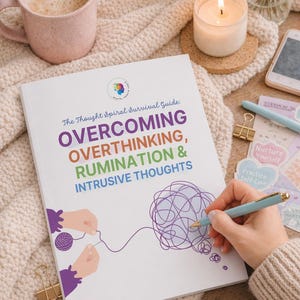 May include: A book titled "OVERCOMING OVERTHINKING, RUMINATION & INTRUSIVE THOUGHTS" is open on a cream-coloured knitted blanket. A person is writing with a light blue pen. A pink mug with coffee, a lit candle, and stickers are also visible.