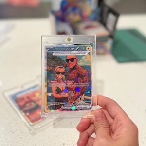 May include: A custom trading card in a clear magnetic protective case featuring an illustration of a couple wearing sunglasses on a beach. The card displays the text A True Love Story ex, 540 HP, Ability Power Couple, and Perfect Match with holographic details.
