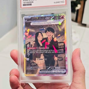 May include: A custom trading card in a clear protective slab featuring an illustration of a couple. The card text reads Happy 1st Anniversary, I Choose You, and I Love You. The slab label includes the text HAPPY 1 YEAR, JESSE & KRISTIE, 1ST EDITION, MINT 10, and I LOVE YOU.