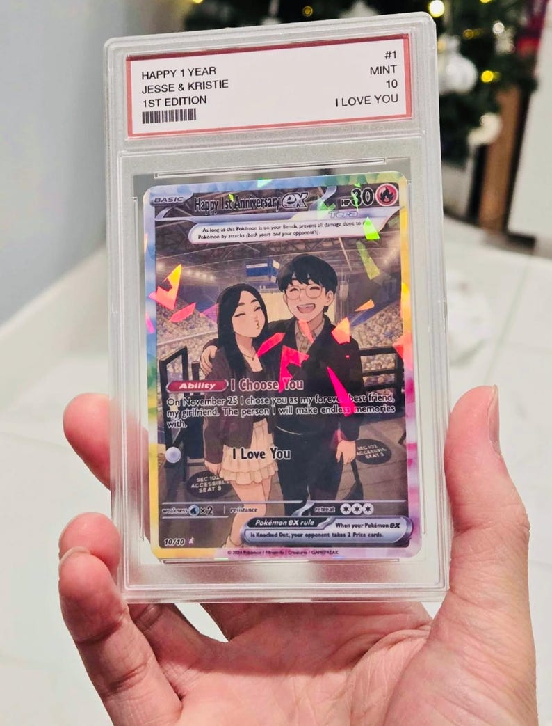 May include: A custom trading card in a clear protective slab featuring an illustration of a couple. The card text reads Happy 1st Anniversary, I Choose You, and I Love You. The slab label includes the text HAPPY 1 YEAR, JESSE & KRISTIE, 1ST EDITION, MINT 10, and I LOVE YOU.
