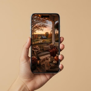 Puede incluir: Un teléfono inteligente que muestra una imagen de alta resolución de un columpio de porche de madera decorado con cojines a cuadros y una manta, con vistas a un paisaje rural otoñal con un granero, calabazas y una taza sobre una mesa al atardecer.