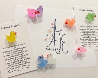 Könnte beinhalten: Eine Sammlung farbenfroher, durchscheinender Pocket Friends in Entenform. Jede Ente hat eine andere Farbe, darunter Gelb, Rosa, Grün, Orange, Blau und Weiß. Das Bild enthält auch Karten mit dem Text "Pocket Friend" und einem Gedicht.