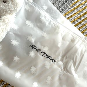 May include: A clear plastic storage bag with a zipper closure and a white star pattern. The bag has the text "Labour Essentials" printed on it.
