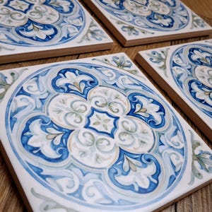 May include: Three square ceramic tiles featuring a central circular motif with intricate blue, white, and light gray scrollwork and floral patterns. Each tile displays a symmetrical design with a white background and a thick, dark blue border.