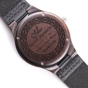 May include: Close-up of a wooden watch with a black leather strap. The watch face is engraved with the name "Elder Scott Johnson", the text "California Fresno Mission", and the dates "2024-2026". The watch has a dark brown finish.