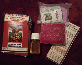 May include: An assortment of spiritual products, including a red box of soap with the text "Sword of Holy Michael Spiritual Soap of Purification", a bottle of oil, a pink package of salt, and a red bar of soap.