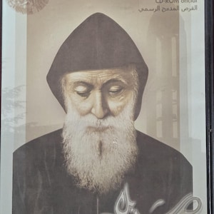 May include: A framed image of Saint Charbel Annaya, a Lebanese Maronite Catholic priest, with a brown background and a silver inscription in the bottom right corner. The text above the image reads "Saint Charbel Annaya", "The official CD-ROM", "Le CD-ROM officiel", "CD-ROM oficial", and "القرص المدمج الرسمي".