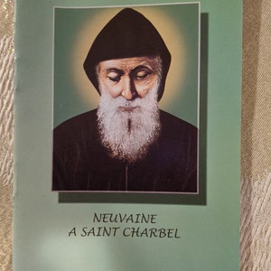 Könnte beinhalten: Ein grünes Büchlein mit einem Bild eines Mannes mit Bart und schwarzer Robe. Der Text auf dem Umschlag lautet "NEUVAINE A SAINT CHARBEL".