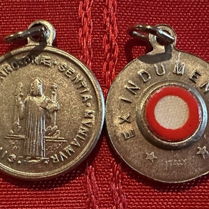 May include: Two silver metal medallions with a loop for hanging. The front of one medallion features a religious figure with a staff and a book. The back of the other medallion has a red and white circle with the text "EX INDUMENTIS" and "MENTIS" around the circle.