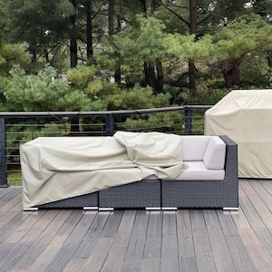 May include: A dark gray outdoor sectional sofa with light beige cushions and a matching cover. The sofa is on a wooden deck with a forest background. A matching cover is on a separate piece of furniture.