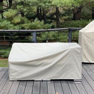 Può includere: Una copertura beige per mobili da esterno per un divano modulare. La copertura è realizzata in materiale resistente all'acqua e ha una cerniera.