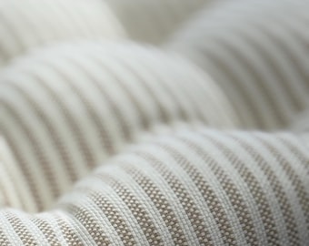 May include: Close-up of a textured fabric with a repeating pattern of thin, vertical stripes in off-white and light brown. The fabric appears to be woven, with a slightly raised texture. The image focuses on the details of the material.
