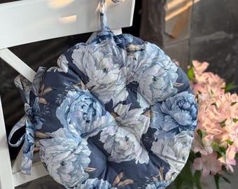 May include: Round chair cushion with a floral pattern in shades of blue and white. The cushion is tied to a white chair with fabric ties. The design features large peony blooms on a dark blue background.