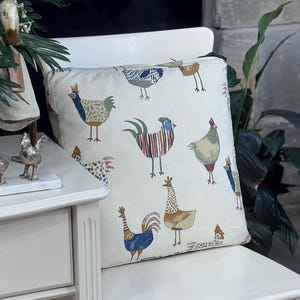 May include: Square decorative pillow with a cream background and a repeating pattern of colorful chickens. The chickens are in various poses and have different patterns and colors, including blue, red, and brown.
