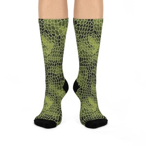May include: Knee-high socks with a green and black camouflage pattern. The socks have black heels and toes. The pattern is a mosaic of irregular shapes in shades of green and black.
