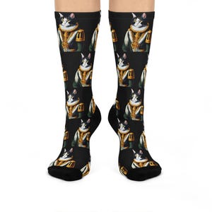 May include: Black socks featuring a repeating pattern of a regal cat wearing a gold and green uniform with a white collar. The cat has black and white fur. The socks are worn on a person's legs.