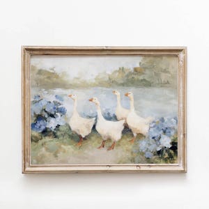 Puede incluir: Pintura enmarcada que representa cuatro gansos blancos cerca de un cuerpo de agua, rodeados de flores azules y vegetación. La obra de arte tiene una estética vintage, con un marco de madera clara. La pintura evoca una escena pastoral serena.