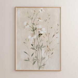 May include: A vertical rectangular wall art piece featuring a painting of delicate white flowers and slender green stems against a soft beige background. The artwork is enclosed in a thin, metallic gold frame that highlights the botanical composition.