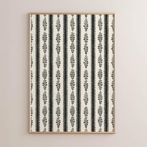 May include: A framed artwork featuring a repeating pattern of vertical black stripes alternating with cream-colored stripes. The black stripes are adorned with a floral design. The frame is a thin, gold color.