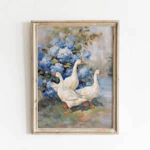 May include: A framed painting depicts three white geese with orange beaks and feet, set against a backdrop of blue hydrangeas and a serene waterscape. The artwork is enclosed in a distressed, light-colored wooden frame.