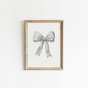 Puede incluir: Una impresión en acuarela enmarcada con un lazo gris. El lazo está centrado sobre un fondo blanco y tiene una apariencia detallada y texturizada. El marco es de color madera clara y natural, lo que añade un toque de encanto rústico a la obra de arte.